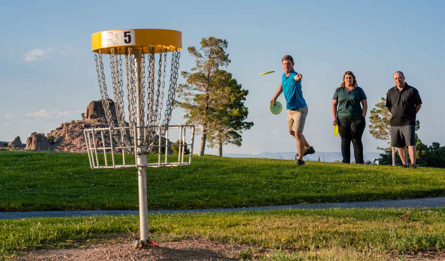three disc golf players tossing into a pin